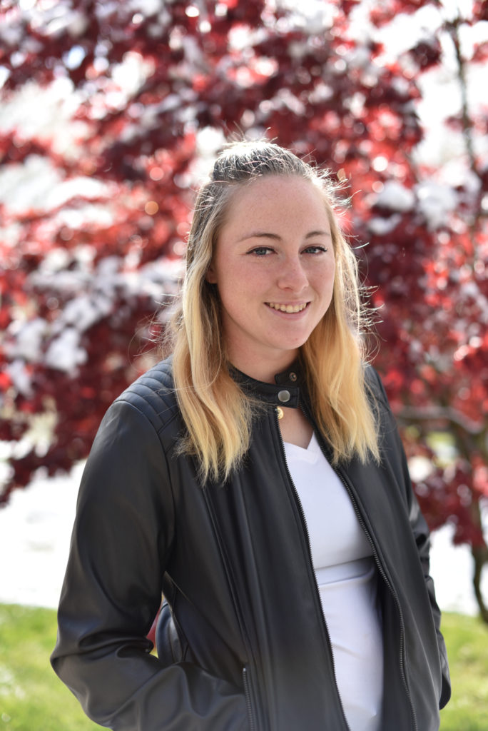 Dayna Dale wear a leather jacket and poses in front of a red leafed tree