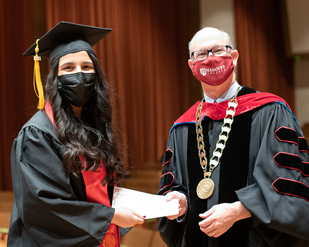 Mayavellie Bochas and President Lake Lambert shake hands while wearing academic regalia
