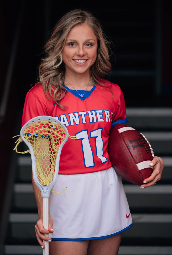 Mya Urba wearing lacrosse uniform and carrying football and lacrosse stick